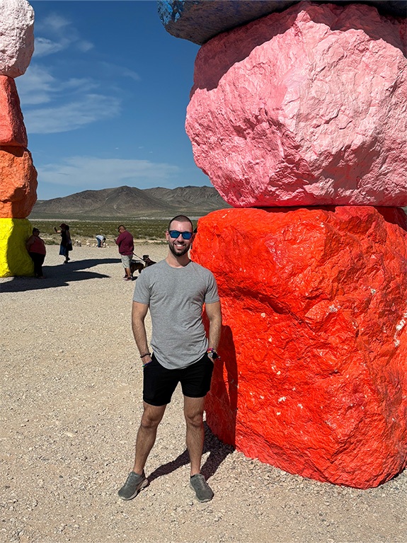 Doctor Snider standing next to colorful boulders wearing sunglasses on a sunny day.